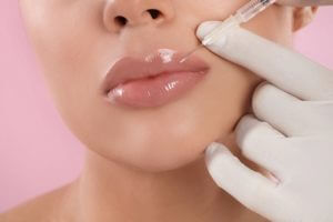 Young woman getting lips injection on pink background